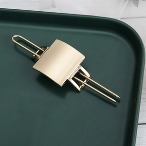 Minimalist gold hollow metal hair clip displayed on a dark green decorative tray