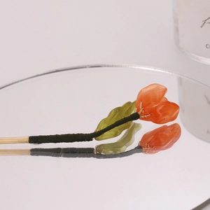 Detailed macro view of tulip hair pin with orange petals and green leaves on gold stem