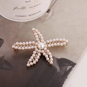 Élégante broche étoile de mer dorée avec perles et strass posée sur un magazine