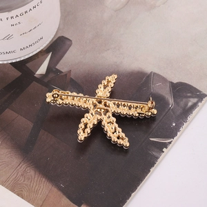 Broche étoile de mer dorée avec perles blanches et texture métallique ajourée