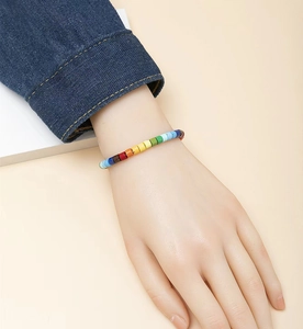Close-up of a colorful rainbow beaded bracelet worn by a model in casual denim jacket