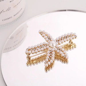 Élégante broche étoile de mer dorée avec perles blanches et cristaux sur miroir
