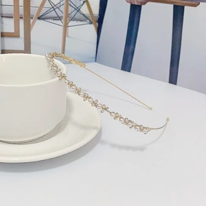 Serre-tête doré délicat avec perles et strass posé sur une tasse en céramique blanche