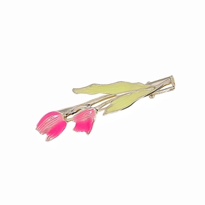 Detail einer rosa Tulpen-Haarklammer mit goldenem Metallboden und grünen Blättern auf Weiß