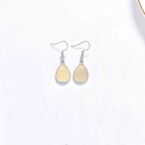 Détail de boucles d'oreilles goutte en résine avec paillettes jaunes sur crochets