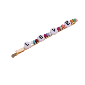 Pasador dorado con cuentas de colores y letras LOVE sobre fondo blanco puro