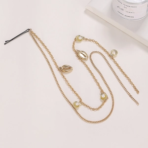 Detail of gold hair chain with metallic shells and pearls on a minimalist background