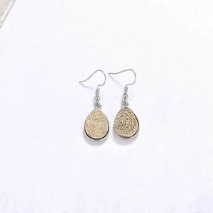 Détail macro de boucles d'oreilles goutte en résine avec paillettes dorées et crochets