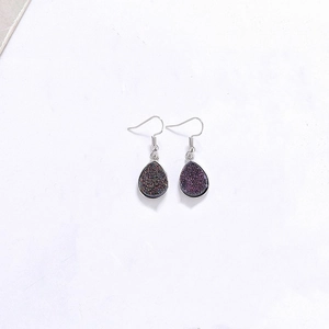Détail de boucles d'oreilles pendantes en résine violet foncé avec crochets argentés