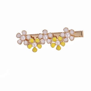 Dettaglio del fermaglio per capelli a fiori dorati con perle bianche e smalto giallo