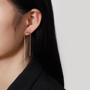 Élégantes boucles d'oreilles dorées en U avec pompons en strass portées par un mannequin