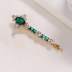 Dettaglio di un fermaglio dorato con cristalli verdi taglio smeraldo e strass bianchi luce