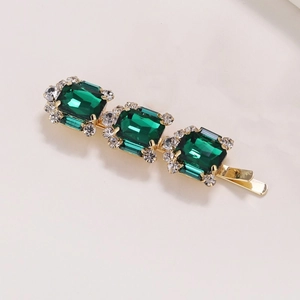 Dettaglio di un elegante fermaglio dorato con tre cristalli verde smeraldo e zirconi lucidi