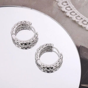 Macro shot of silver hollow-out braided wave hoop earrings with mirror reflection