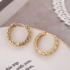 French vintage style gold hollowed hoop earrings with geometric wave pattern on a ceramic plate