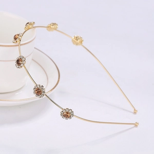 Golden metal sunflower headband with amber crystals and rhinestones on a white cup