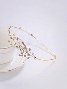 Détail d'un serre-tête doré avec feuilles et strass posé sur une tasse en porcelaine
