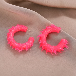 Neon pink C-shape stud earrings with 3D spiky texture on brown fabric background