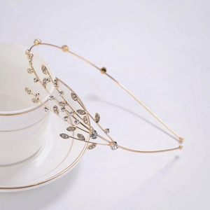 Serre-tête élégant en feuilles dorées avec strass et perles posé sur une tasse blanche