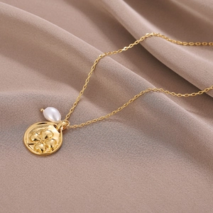 Collier avec pendentif trèfle doré et perle blanche sur fond de soie élégant