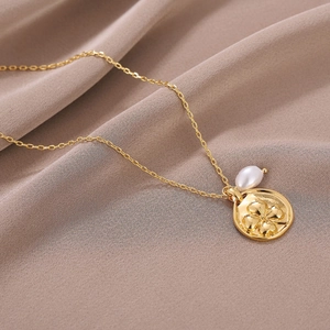 Détail du collier avec pendentif pièce trèfle et perle baroque sur tissu satiné élégant