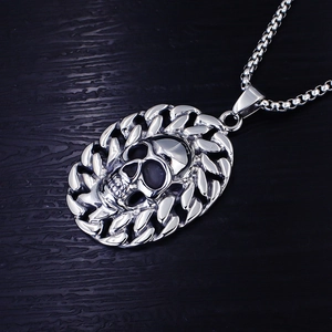 Macro detail of silver skull pendant with cuban chain border on dark wood background