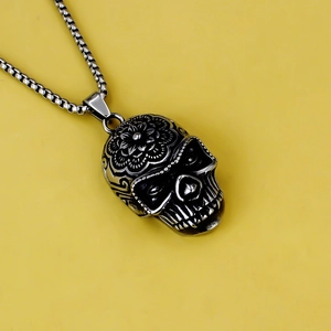 Detail of vintage stainless steel skull pendant with floral carvings on yellow backdrop