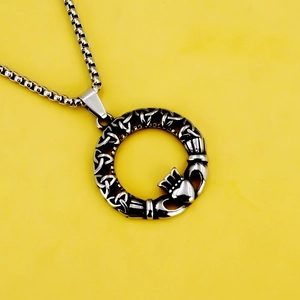 Silberne Halskette aus Edelstahl mit Claddagh-Keltischer-Knoten-Anhänger auf Gelbem Hintergrund