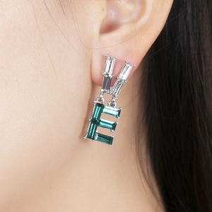 Detail of asymmetric emerald green crystal letter E earrings worn by a model
