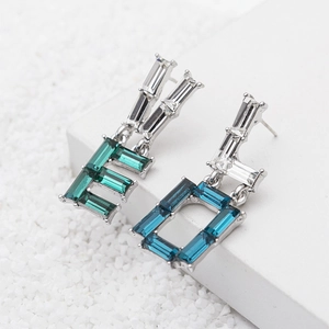 Asymmetric silver earrings with emerald and blue emerald-cut crystals on stones background