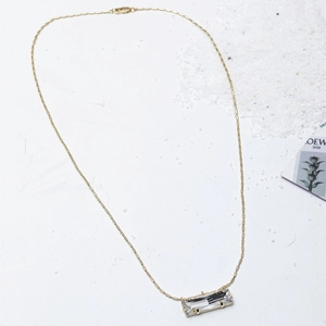 Collier doré minimaliste avec pendentif en pierre transparente rectangulaire sur fond texturé blanc