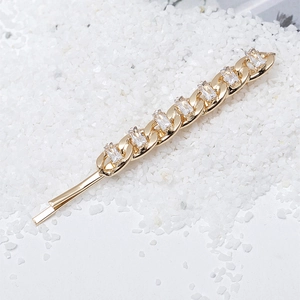 Elegant gold metal chain hair clip with sparkling zircon stones on white pebbles