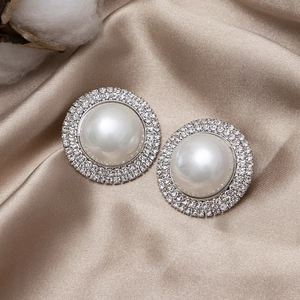 Luxurious pearl stud earrings with sparkling crystals on champagne silk background