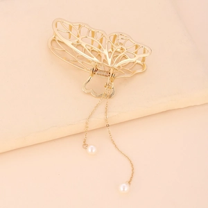 Détail de la pince à cheveux papillon dorée avec pompon perle sur support beige