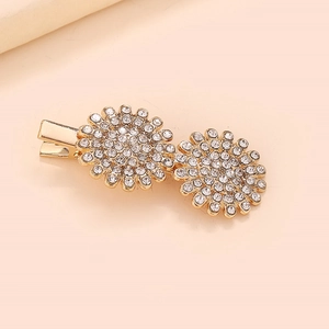 Détail de deux barrettes marguerites dorées avec strass brillants sur fond rose clair