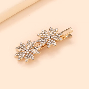 Détail d'une pince à cheveux flocon de neige dorée avec strass sur fond rose doux