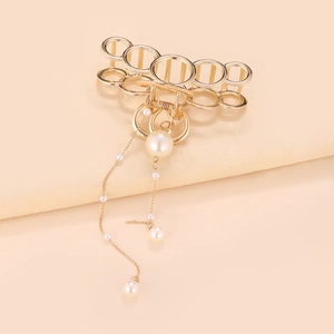 Détail de la pince à cheveux dorée avec boucles métalliques et pompons de perles
