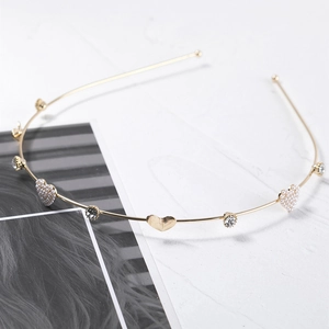 Golden metal headband with pearl heart and rhinestone detail on marble surface