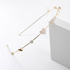 Detailed macro view of a thin gold metal headband featuring a pearl heart and rhinestones