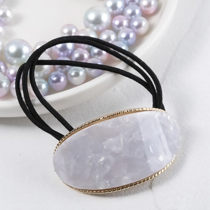 Macro detail of oval purple marble acetate hair tie with golden metallic frame edge