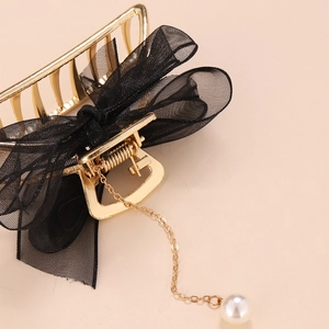 Détail de la pince à cheveux dorée avec nœud en maille noire et pendentif en perle