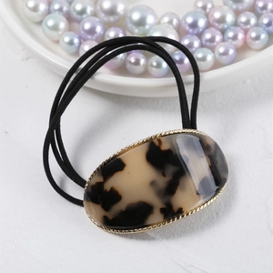 Close-up of tortoiseshell acetate oval hair tie with gold trim and black elastic band