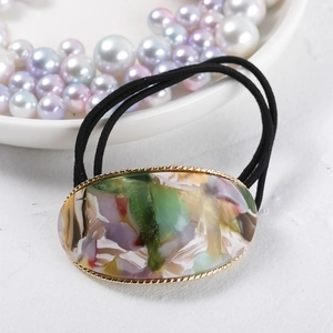 Detail of oval marble acetate hair tie with golden woven metal border and black elastic band