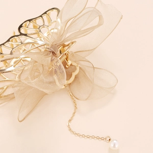 Détail d'une pince à cheveux dorée avec nœud en organza et élégant gland perlé