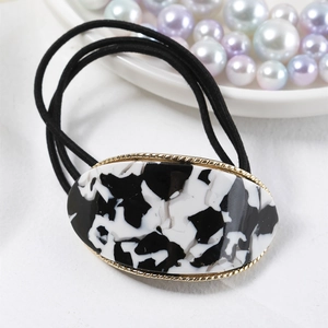 Detail of oval black and white marble pattern hair tie with gold trim and elastic bands