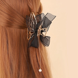 Détail d'une pince à cheveux à nœud avec ailes dorées et pompon de perle blanche