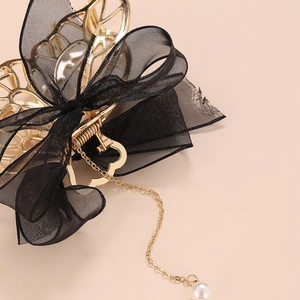 Détail de pince à cheveux dorée avec nœud en maille noire et gland perle élégant