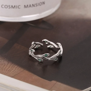 Detail eines silbernen Olivenzweig-Rings mit grünen Zirkonia auf dunklem Papier
