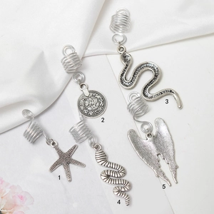 Détail de cinq bijoux de cheveux argentés avec pendentifs étoile, pièce, serpent et ailes
