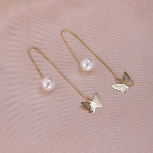 Detailed view of long gold chain earrings with butterfly pendant and pearl on pink silk